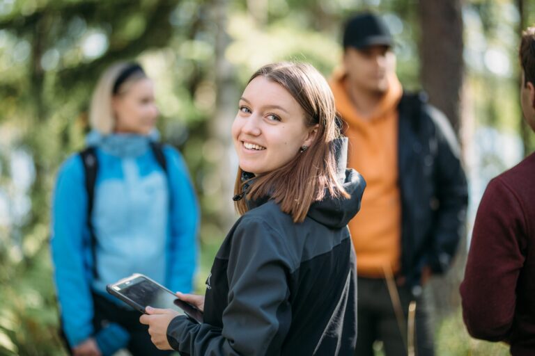 Students in the woods with a tablet.