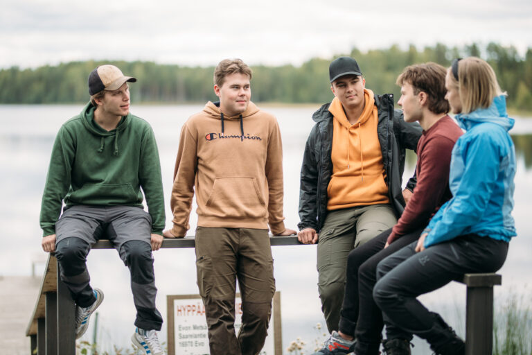 A group of people sitting next to a lake/Ryhmä ihmisiä istuu lähellä järveä