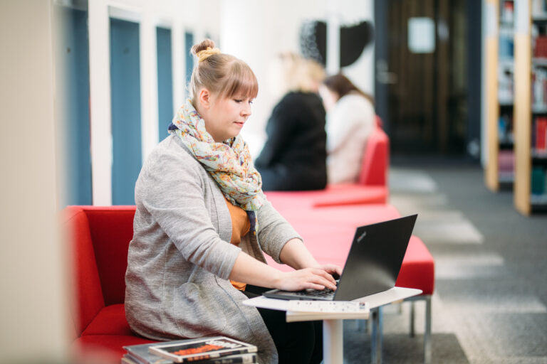 Woman working with a computer on hallway/Nainen työskentelee tietokonella käytävällä