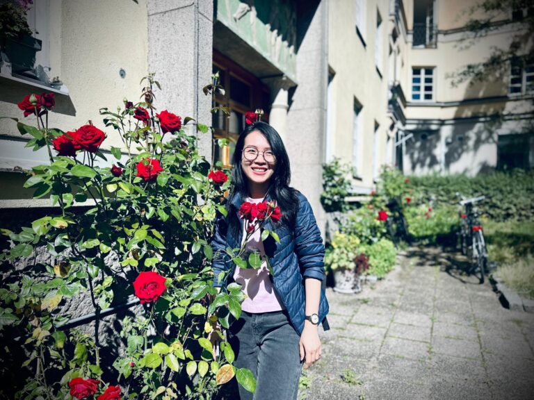 Computer Applications student outdoors next to flowers.