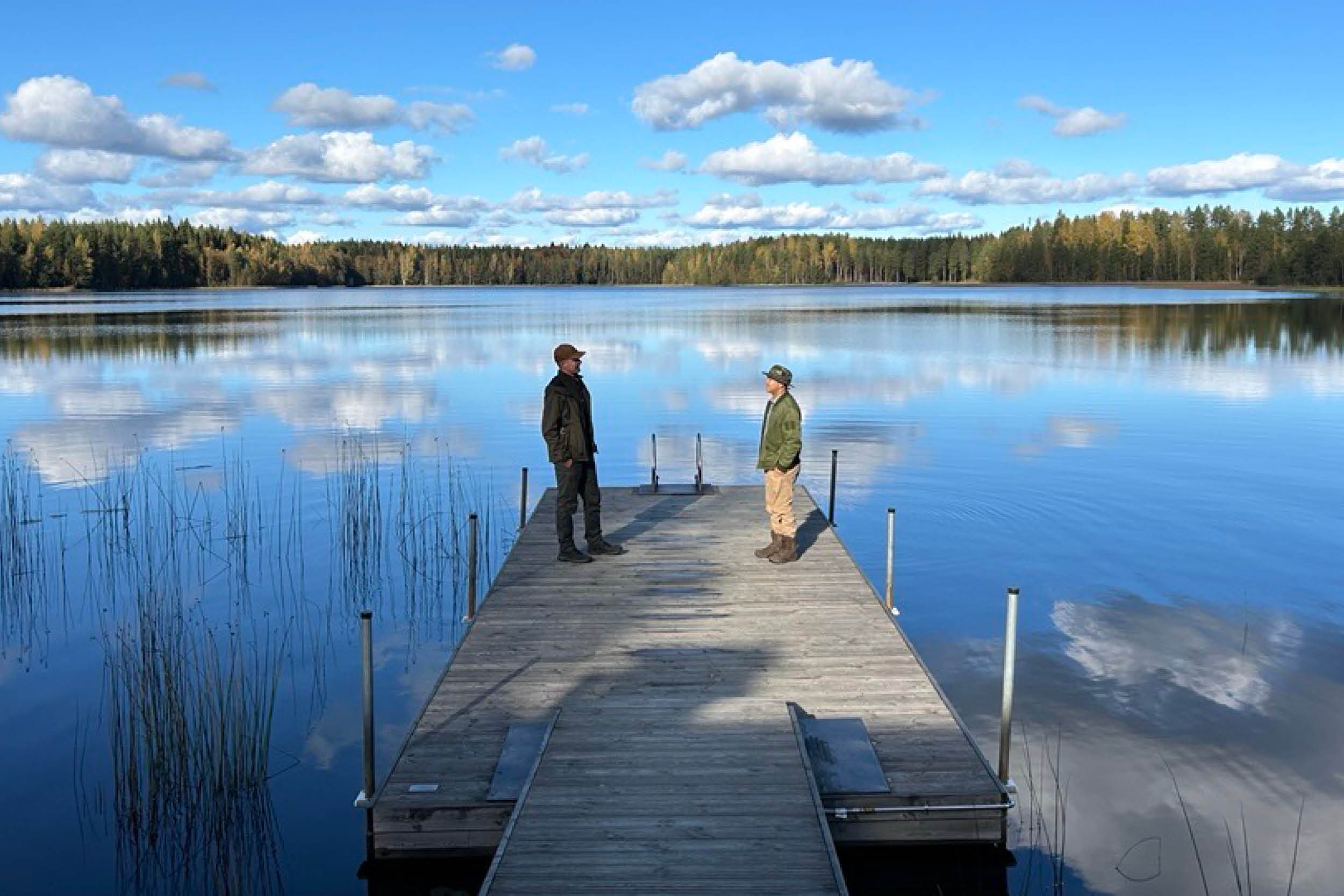 Kaksi opiskelijaa laiturilla sininen järvi taustalla