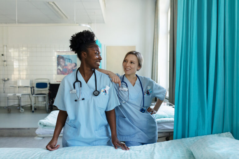 Kaksi sairaanhoitajaa sängyn vieressä/ Two nurses next to a bed